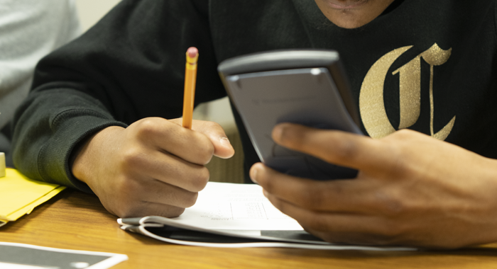 A student holds a pencil and a calculator.