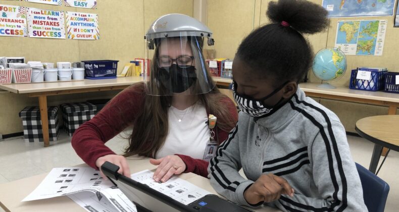 teacher wearing face shield and mask teaching student wearing mask