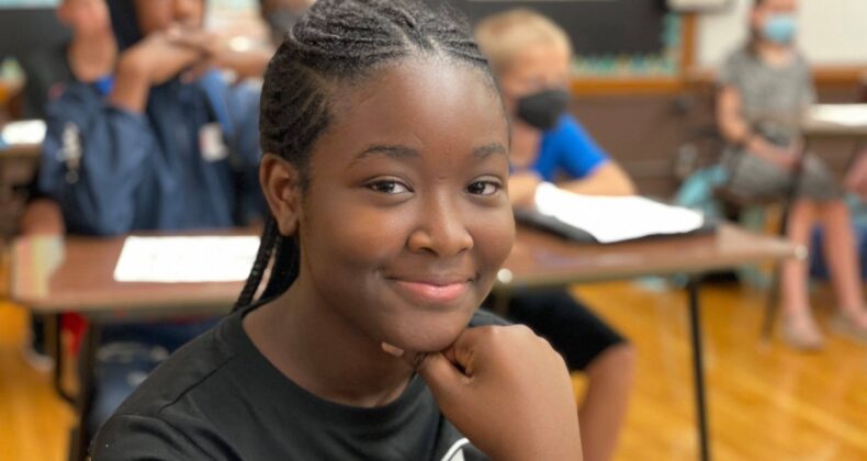 student smiling at desk in classroom