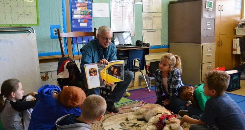 volunteer with dog reading to group of students